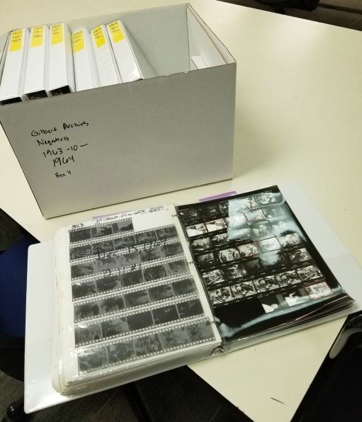 A binder full of 35mm photo negatives and contact sheets sits in front of a box full of binders