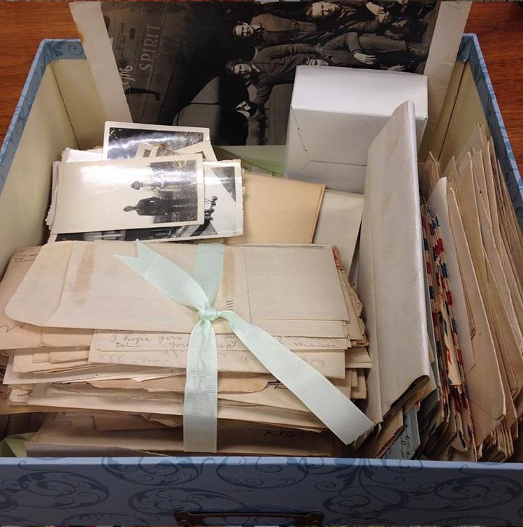 A small blue box is filled with bundles of letters tied with ribbons and stacks of black and white photographs